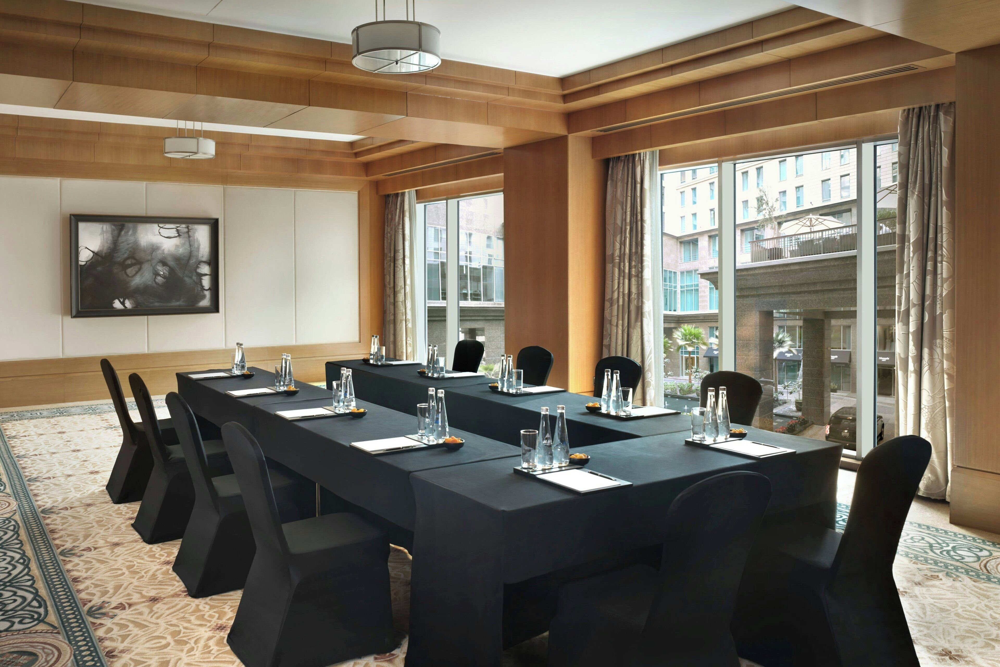 A conference room with a long table, chairs, and a large window with a view of buildings.