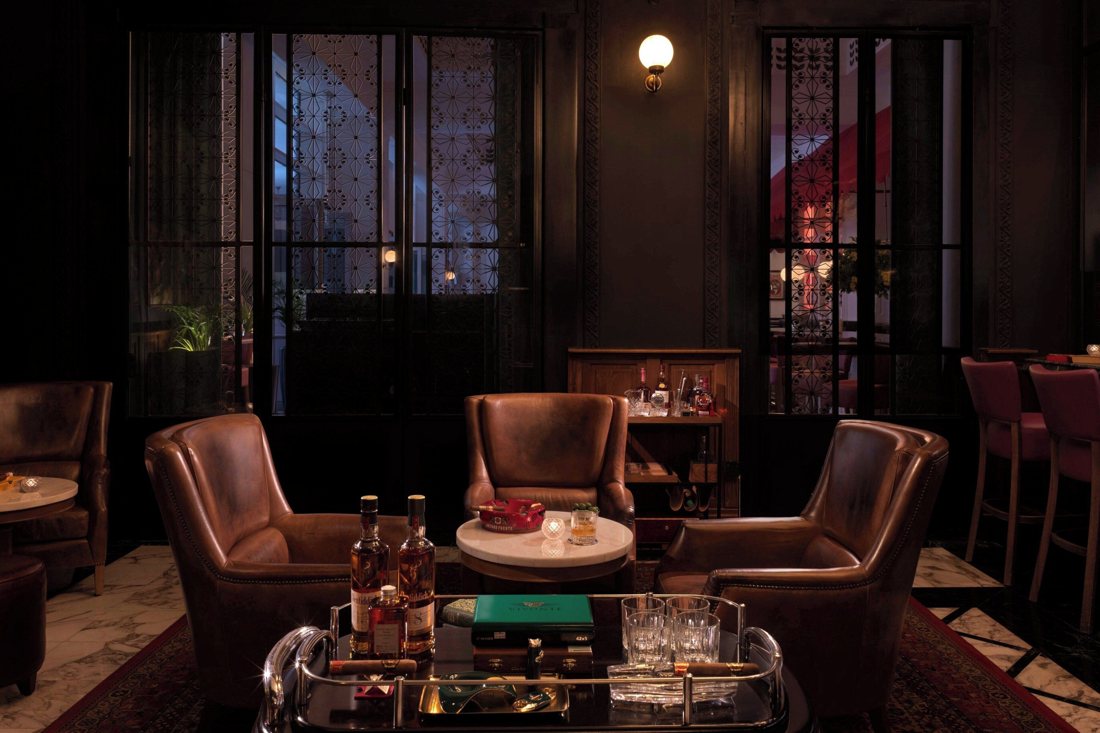 A dimly lit room with leather chairs, a small round table, and a bar area with bottles and glasses.