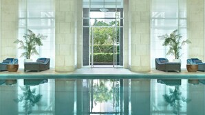 A poolside area with lounge chairs and potted plants, a clear view of greenery outside, and a tiled wall.