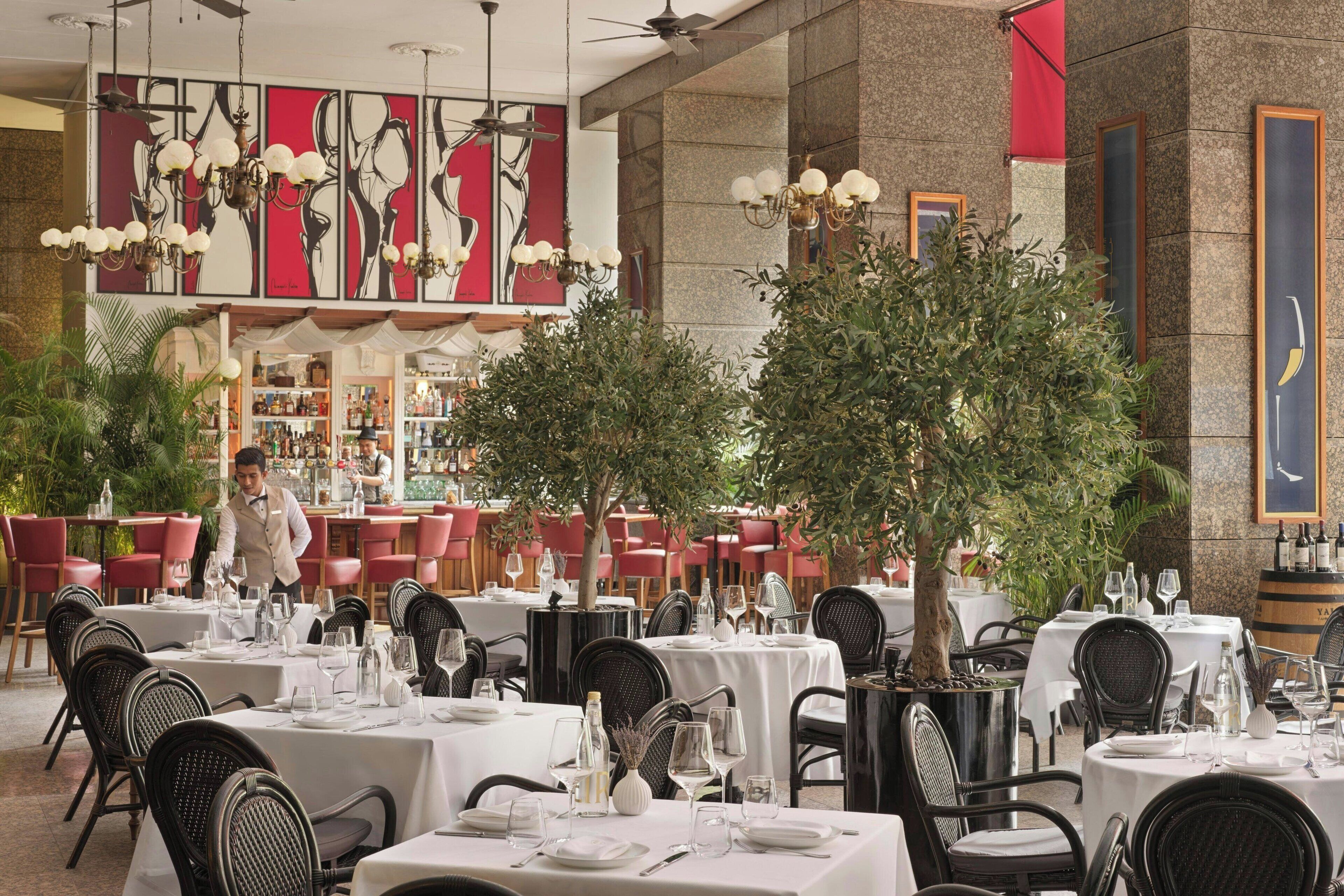 A restaurant with tables set for dining, a bartender, and a bar area.