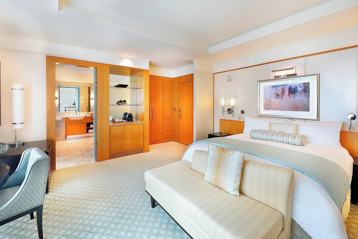 Quarto de hotel com uma cama grande, um sofá, uma escrivaninha, um espelho e um guarda-roupa.