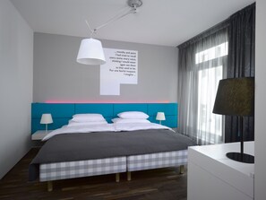 Ein modernes Hotelzimmer mit einem großen Bett, einem Kopfteil mit blauer Neon-Akzent, einem Nachttisch mit Lampe und einer Wand mit einem Zitat.