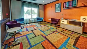A hotel lobby with a colorful carpet, two blue armchairs, a purple armchair, a small round table, and a reception desk with a decorative item. - Fairfield Inn & Suites Oklahoma City Airport (Oklahoma City)