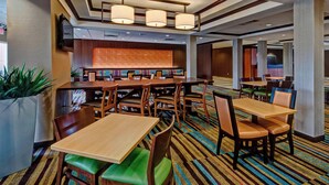 A hotel lobby with multiple seating areas, including tables and chairs, a large screen, and a patterned carpet. - Fairfield Inn & Suites Oklahoma City Airport (Oklahoma City)