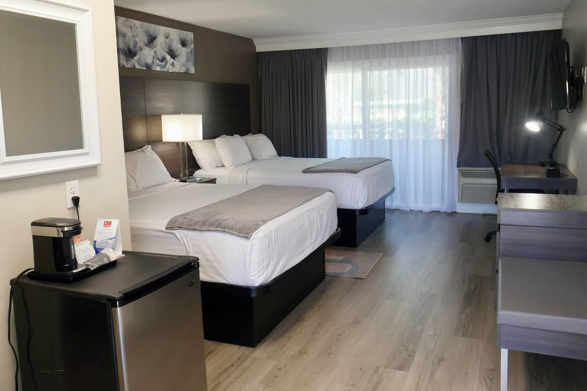 Habitación de hotel con dos camas, un escritorio, una silla, una cafetera y un televisor.