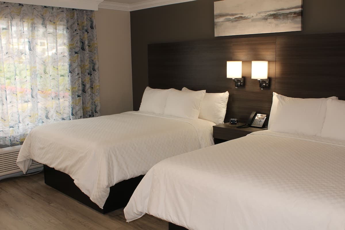 Habitación de hotel con dos camas, un ventanal con cortinas, un teléfono en la pared y un cuadro sobre las camas.