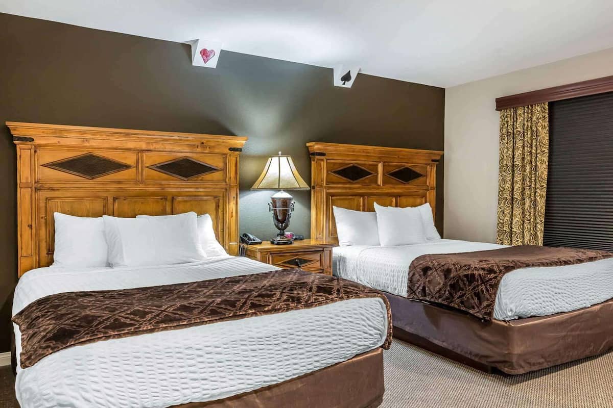 Habitación de hotel con dos camas, cabeceros de madera, una mesita de noche con lámpara y una ventana con cortinas.