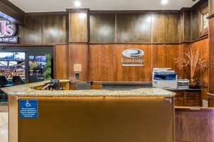 Un área de recepción con paneles de madera, un letrero que dice 'Econo Lodge', un mostrador de recepción y un cartel de accesibilidad para sillas de ruedas.