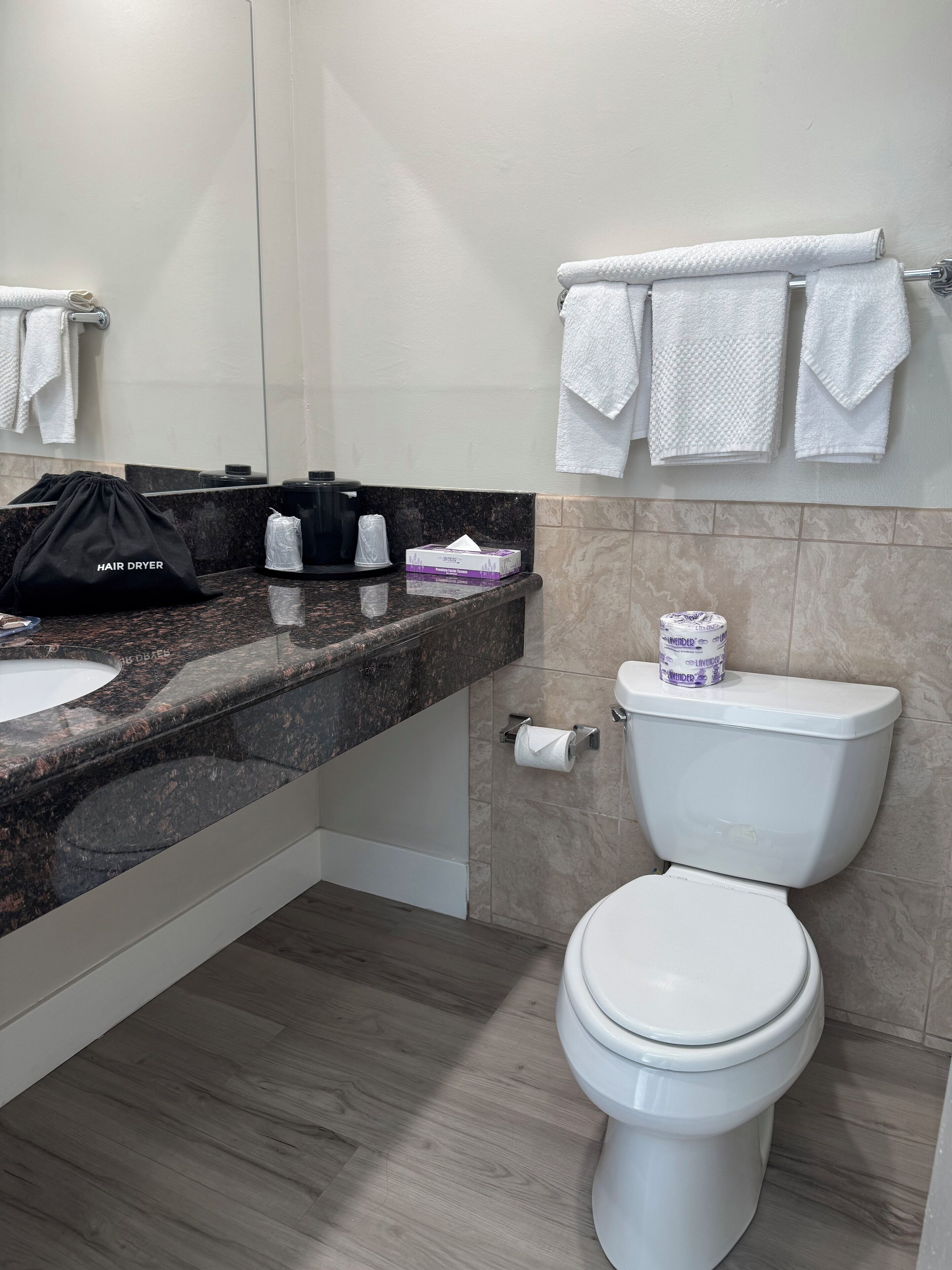 Un baño moderno con encimera de granito, inodoro blanco y toallero con varias toallas.
