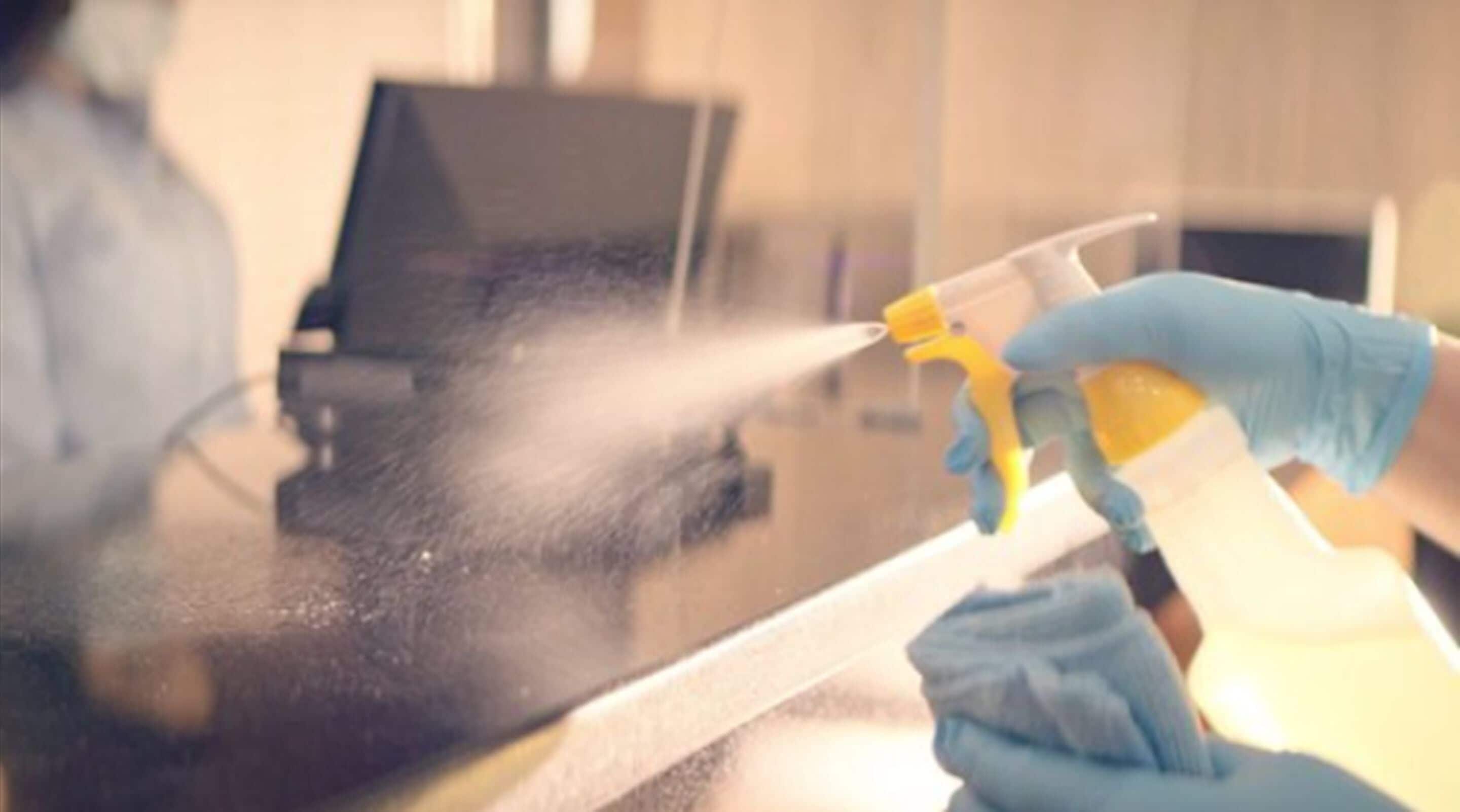 Una persona limpia una superficie de vidrio con un atomizador.