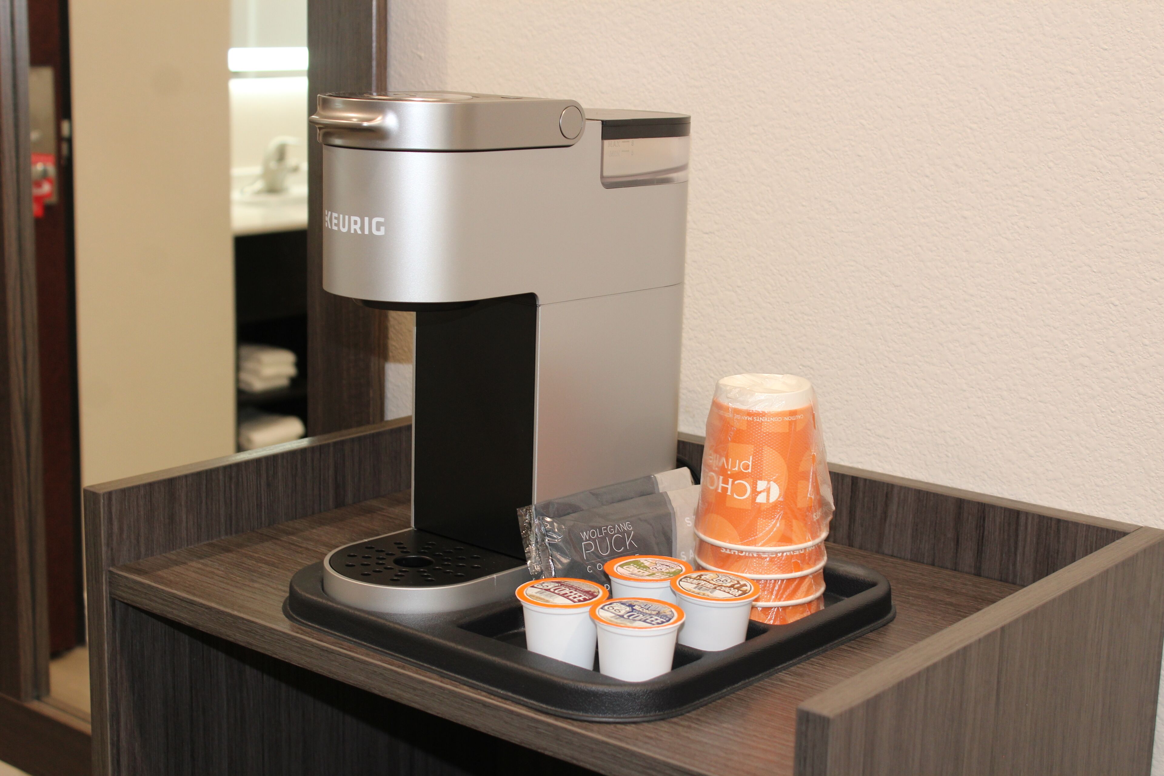 A coffee machine with disposable cups and a bottle of orange juice on a tray.