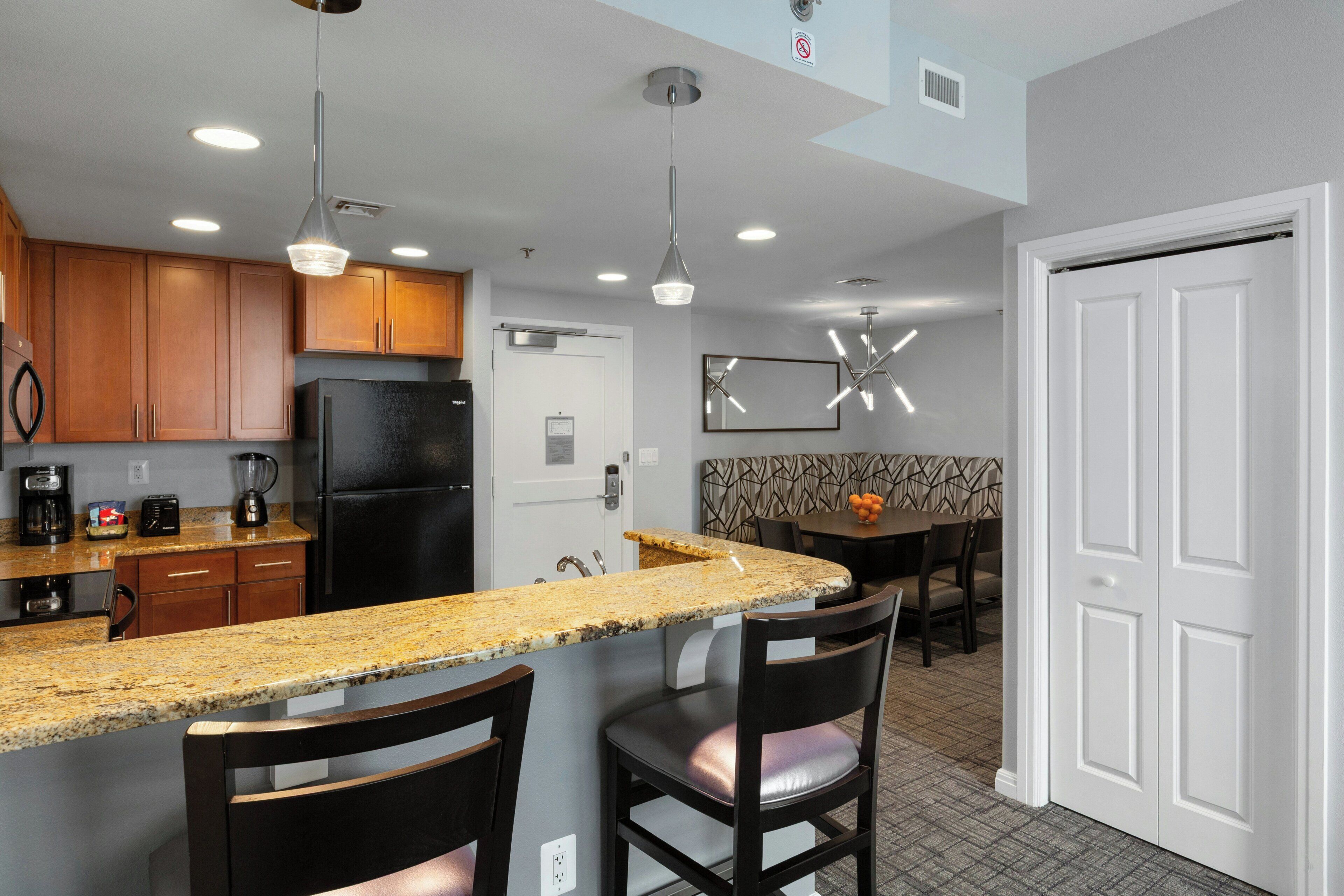 A modern kitchen with granite countertops, wooden cabinets, a black refrigerator, and pendant lighting.