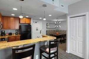 Una cocina moderna con encimeras de granito, armarios de madera, refrigerador negro e iluminación colgante.