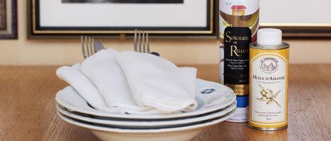A table with a bowl of folded white napkins, a bottle of extra virgin olive oil, and a can of almond oil.
