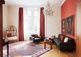 Uma sala de estar com uma janela grande, um candelabro, um sofá, uma poltrona e um tapete.