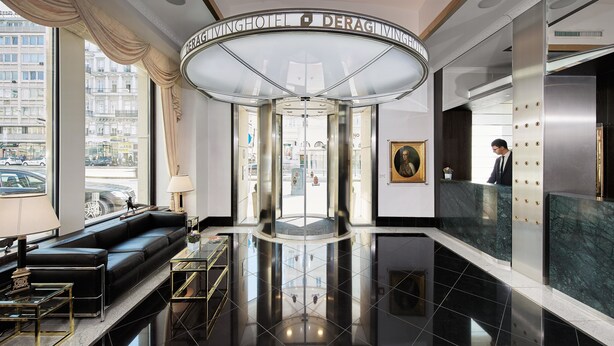 A hotel lobby with a revolving door, a reception desk, a black leather sofa, and a glass coffee table. - Living Hotel an der Oper (Vienna)