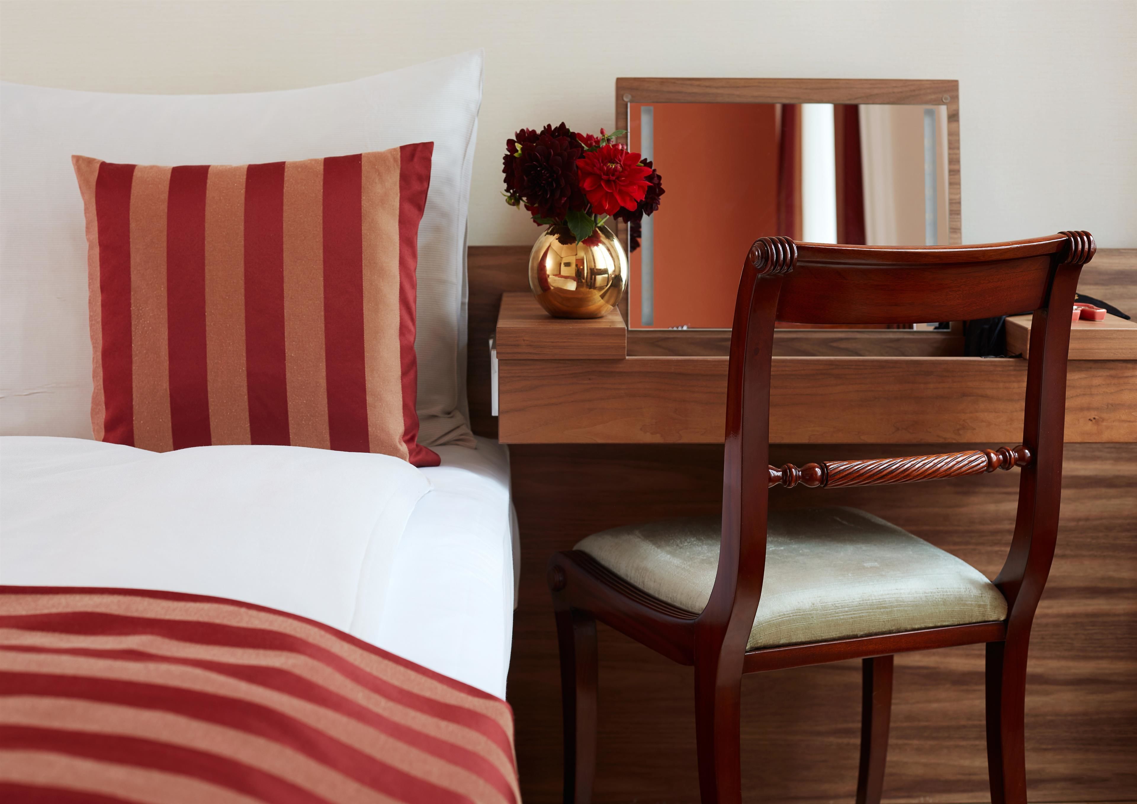 Una habitación de hotel con una cama, una silla de madera, un escritorio y un espejo.