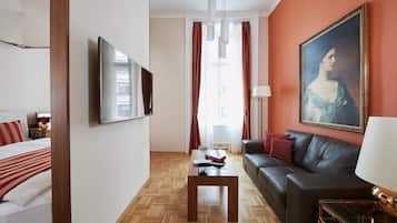 Habitación de hotel con cama, sofá, mesa de centro, un cuadro y ventana con cortinas.