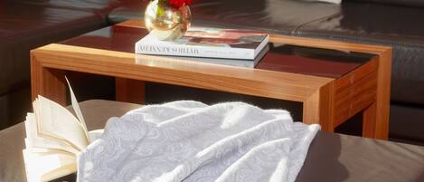 A reading area with a sofa, a coffee table, a book, a vase with flowers, and a blanket.