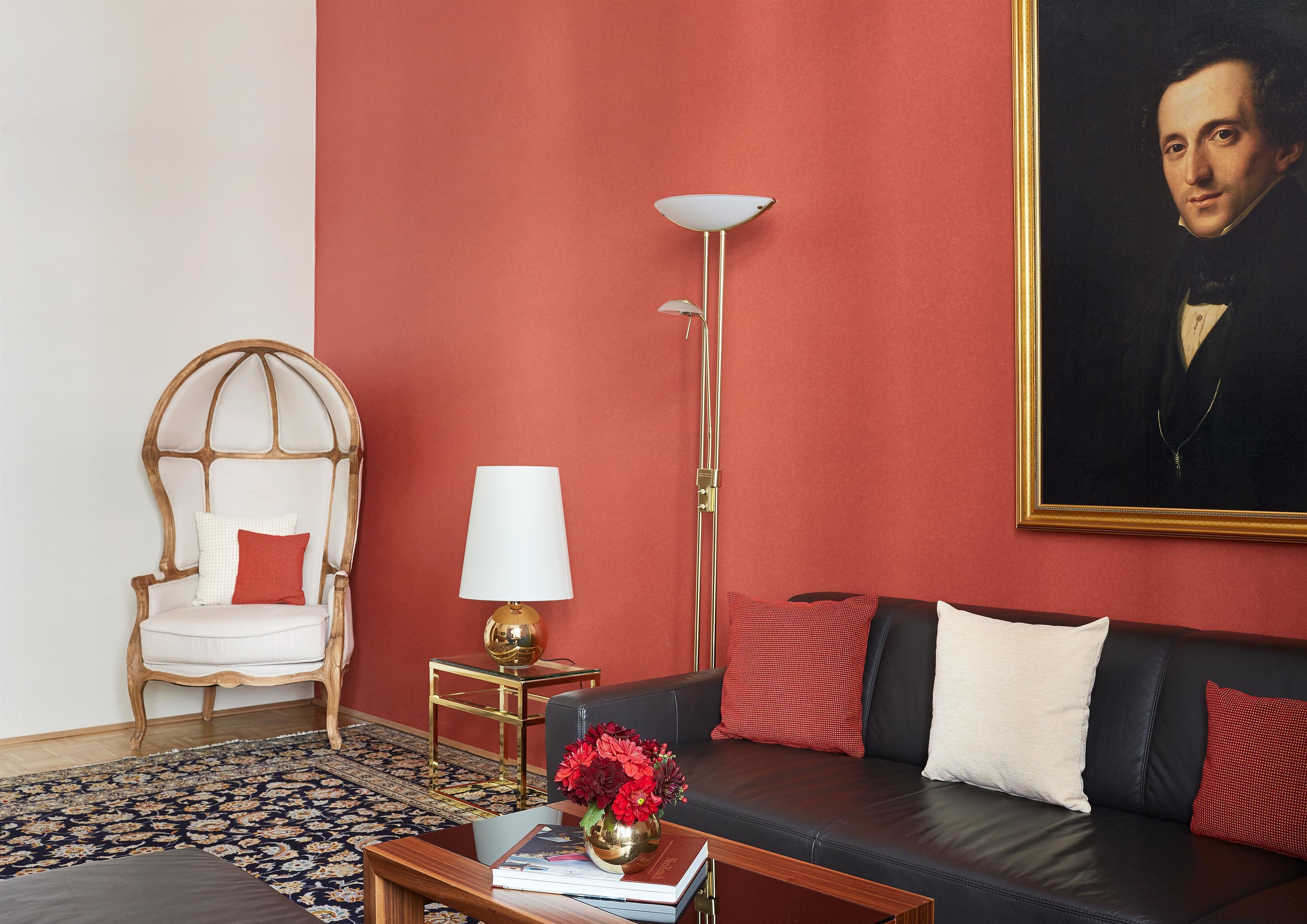 Un soggiorno con una parete rossa, una poltrona bianca, un divano nero, una lampada da terra e un quadro.