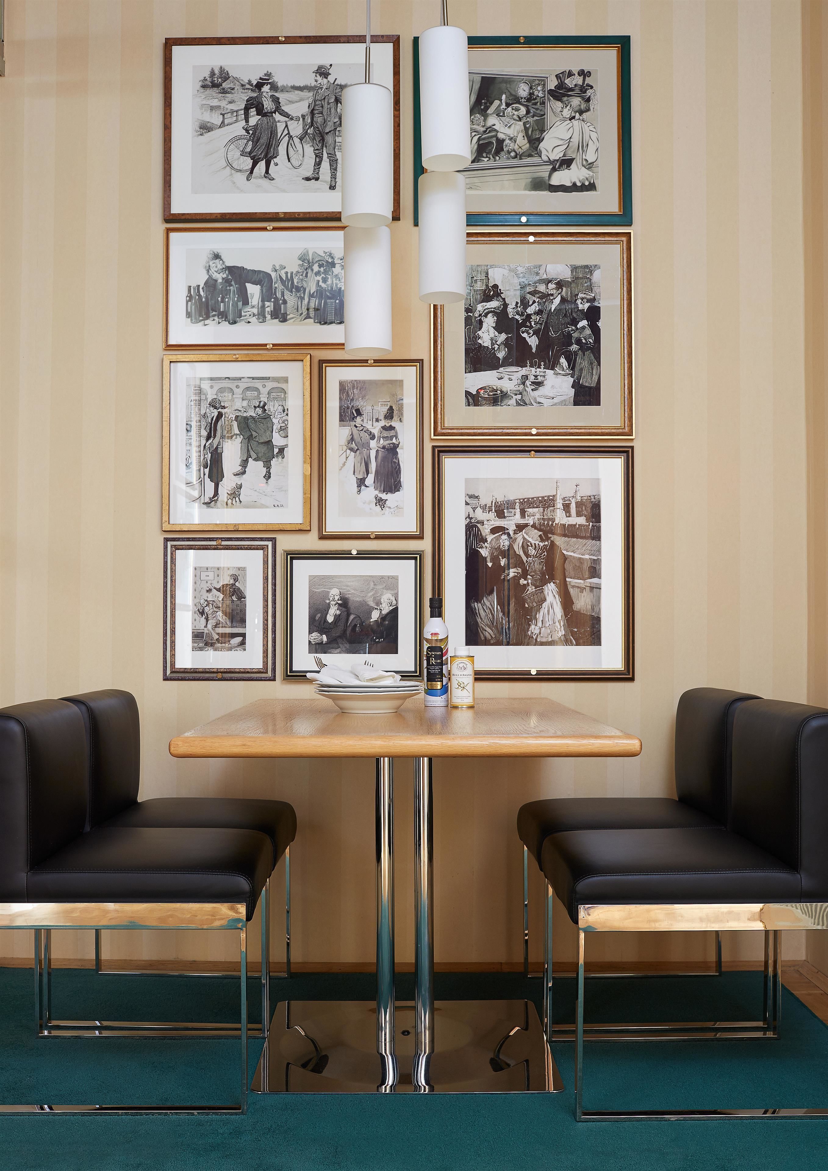 A room with a wooden table, two black leather chairs, and a wall decorated with framed black and white photographs.