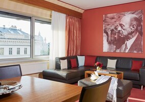 Uma sala de estar moderna com um sofá de couro, uma mesa de centro de madeira e vista para um horizonte urbano através de amplas janelas.