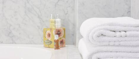 A bathroom with a marble sink, a stack of white towels, and two toiletry bottles on a yellow box.