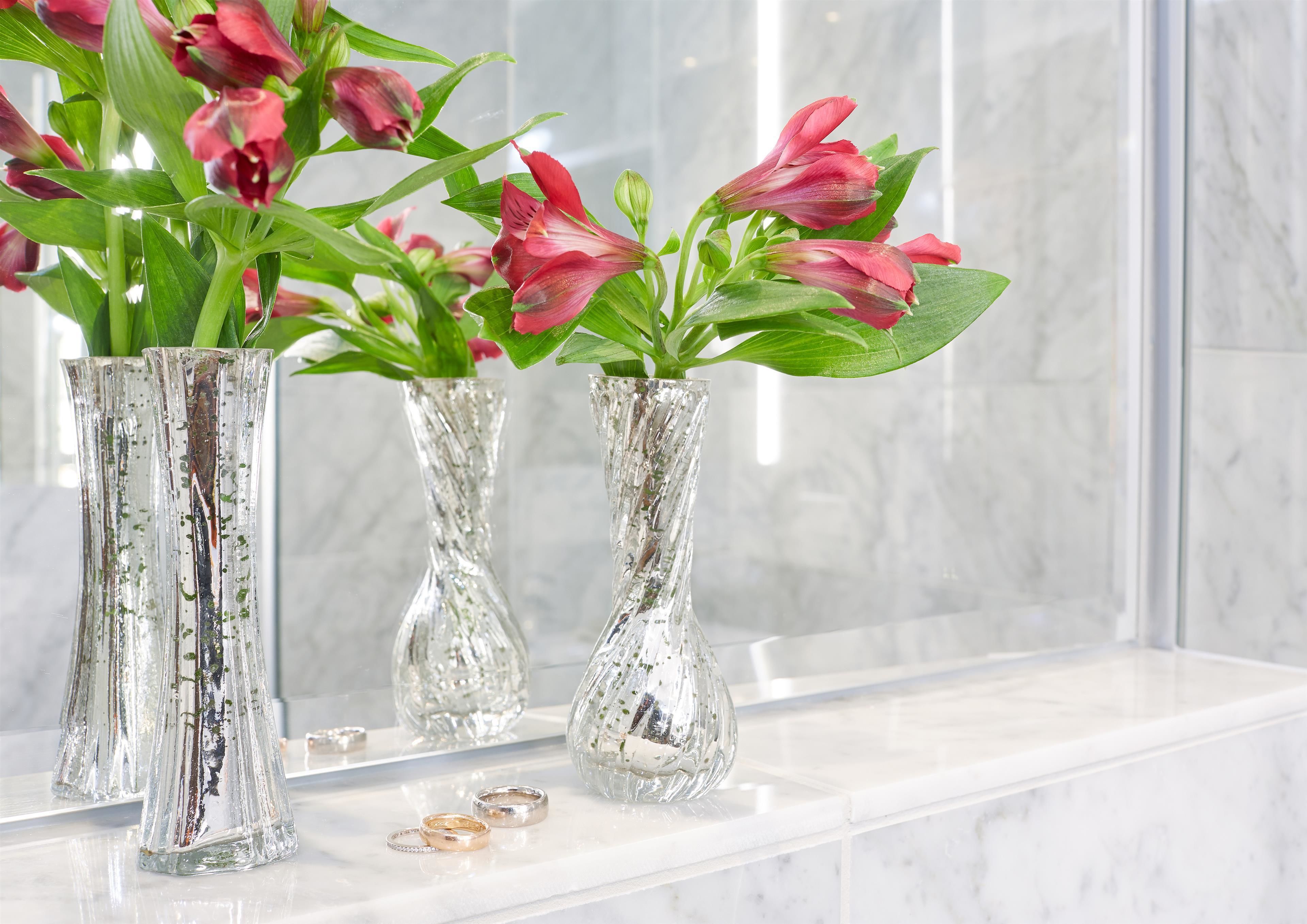Drei Glasvasen mit roten Blumen auf einer Marmorarbeitsplatte.