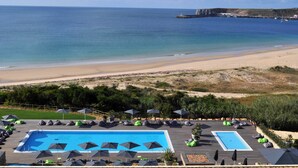 A pool area with lounge chairs and umbrellas, a beach view, and a rocky coastline. - Martinhal Sagres Beach Family Resort (Vila do Bispo)