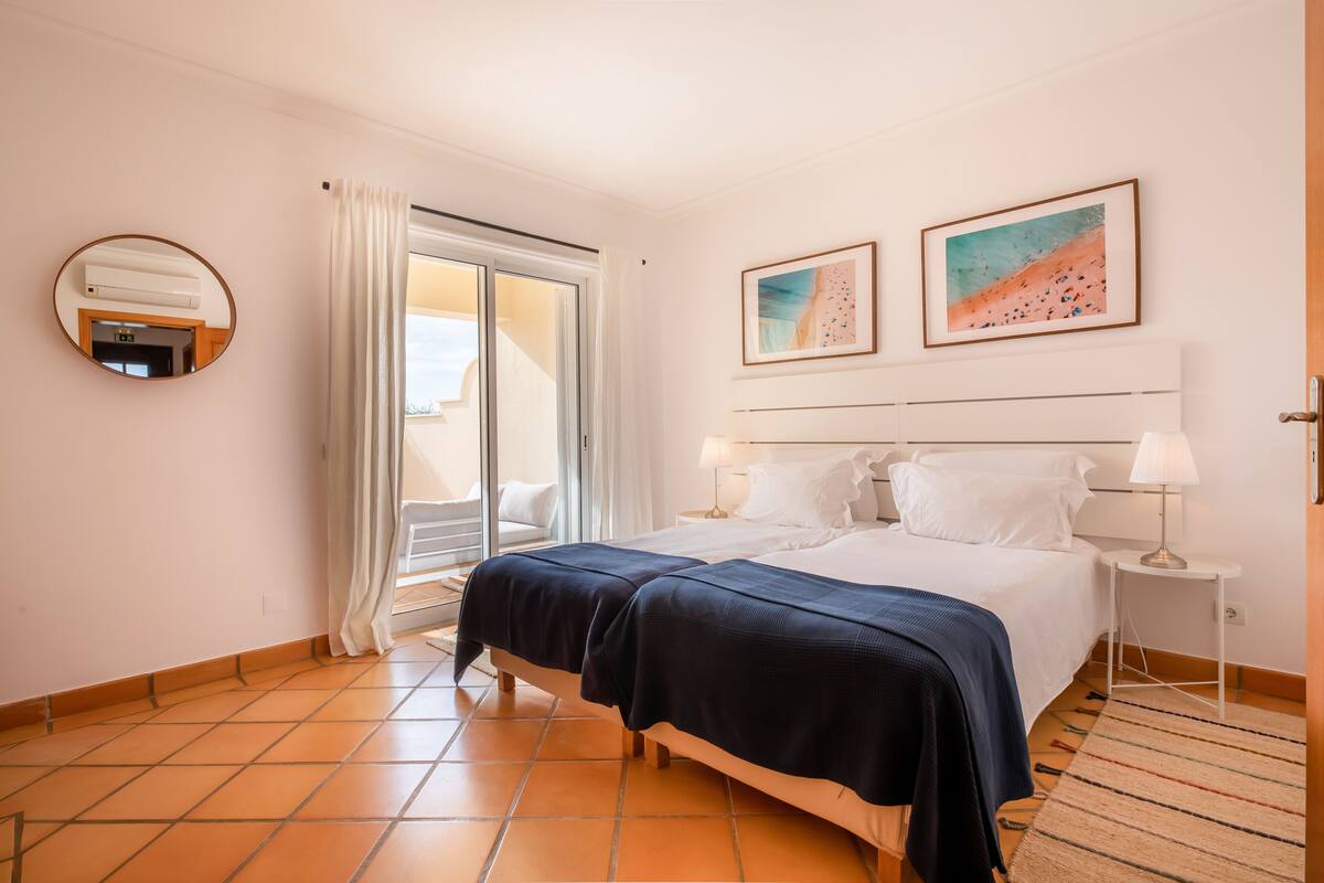 A hotel room with a bed, two bedside tables, a mirror, and a window with curtains.