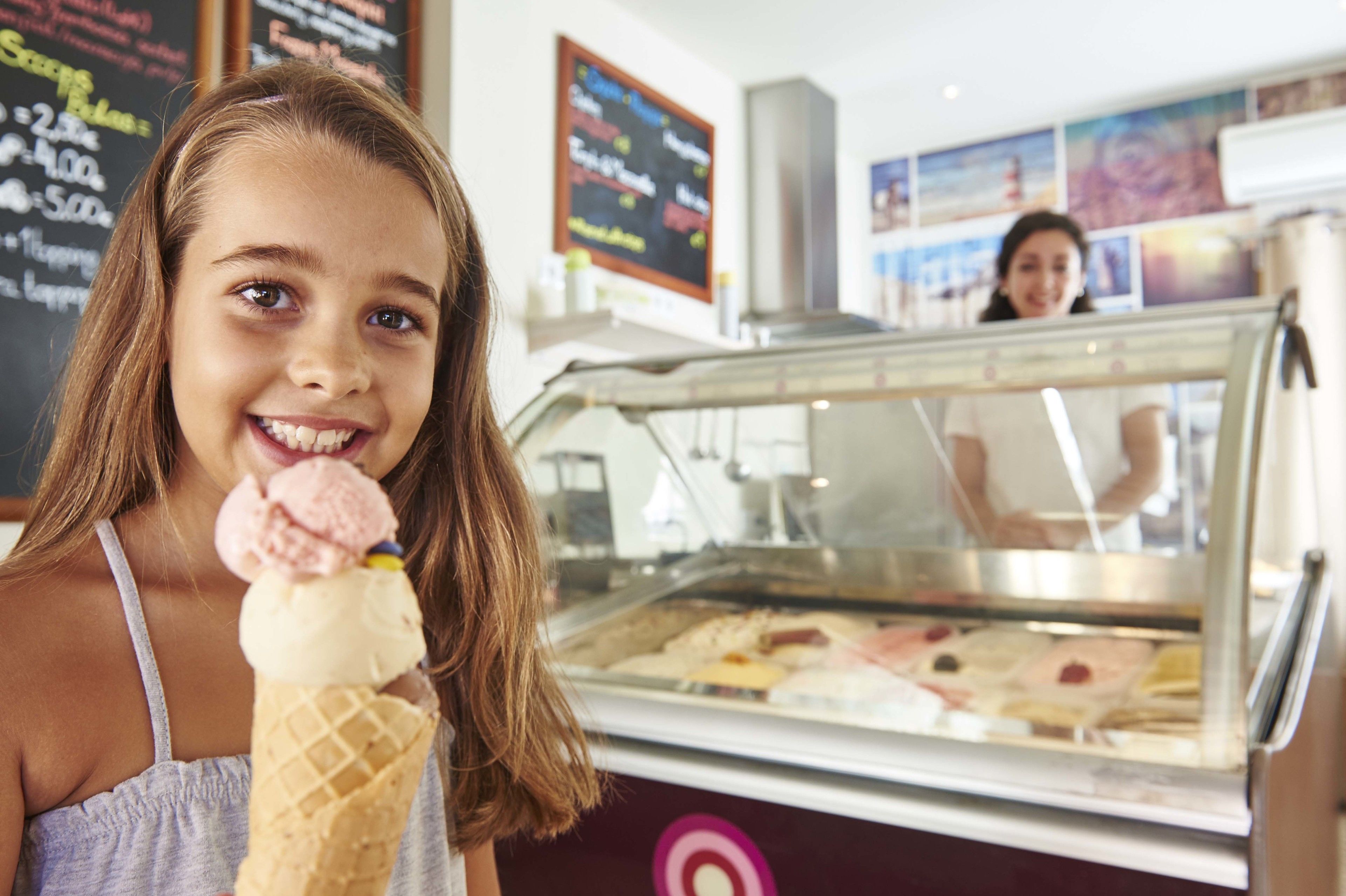 A person holding an ice cream cone in front of an ice cream display.