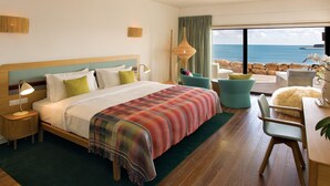 A hotel room with a large bed, a view of the ocean, a dining area, and a seating area with a view.