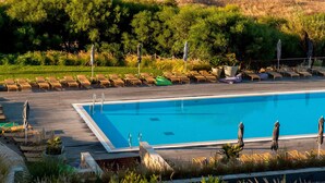 Un área de piscina con sillones y sombrillas, una playa con sombrillas y tumbonas, y vistas al mar y a los acantilados.