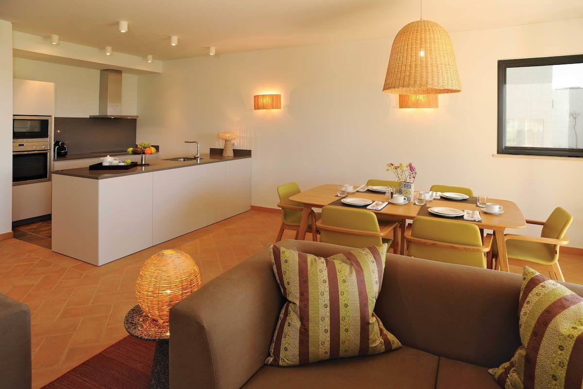 A modern kitchen with a central island, dining area with chairs, and a sofa with striped cushions.