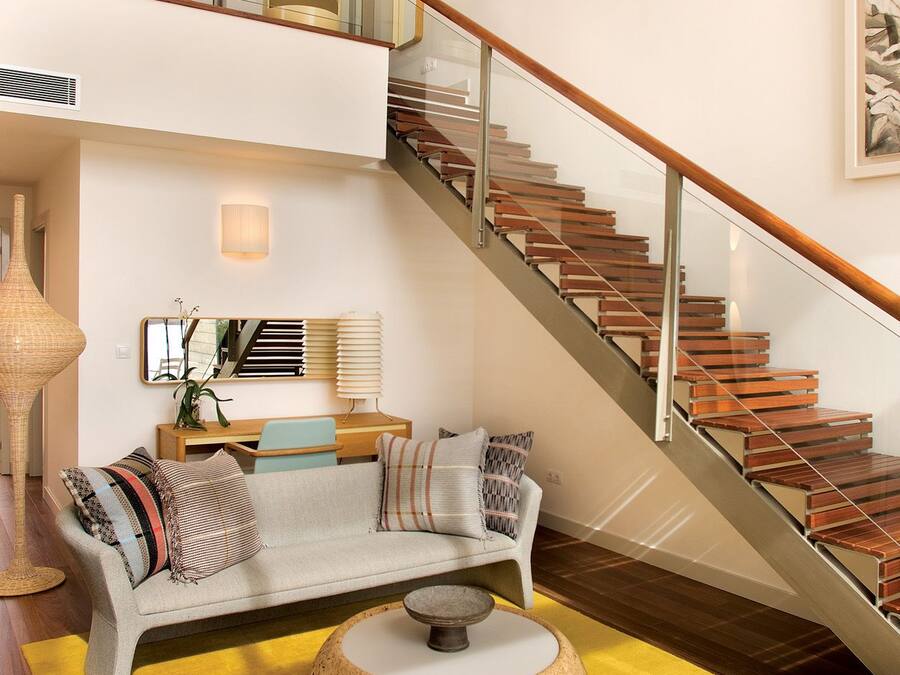 Una sala de estar moderna con una escalera, un sofá, una mesa de centro redonda y una alfombra amarilla.