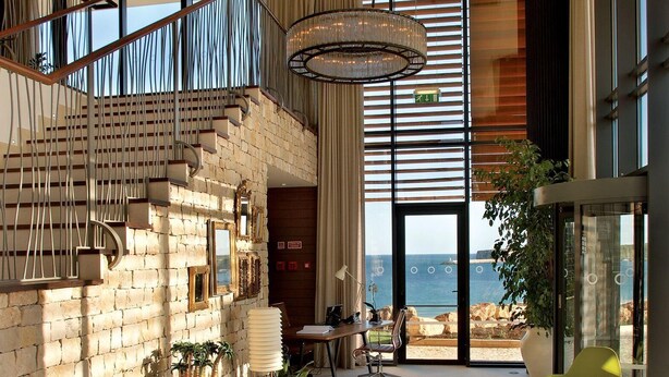Un espacio habitable amplio con una escalera, un gran ventanal con vistas al mar y una moderna lámpara de araña.