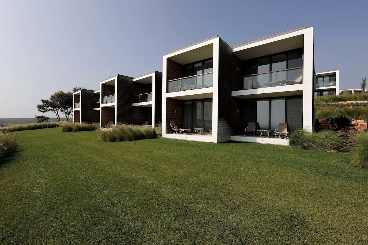 A modern multi-story residential building with balconies, a well-maintained lawn, and a clear view of the surrounding landscape.