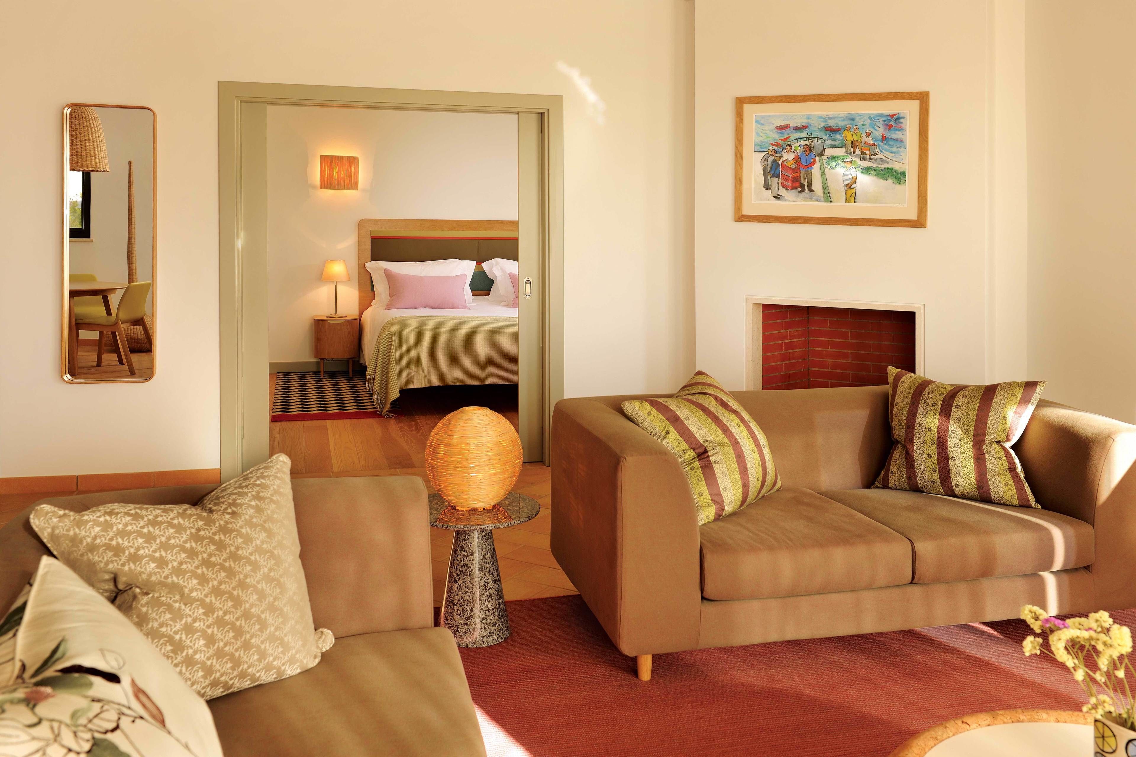 Ein Hotelzimmer mit einer Couch, einem kleinen Tisch mit Lampe, einem Spiegel, einem Gemälde und einem Kamin.