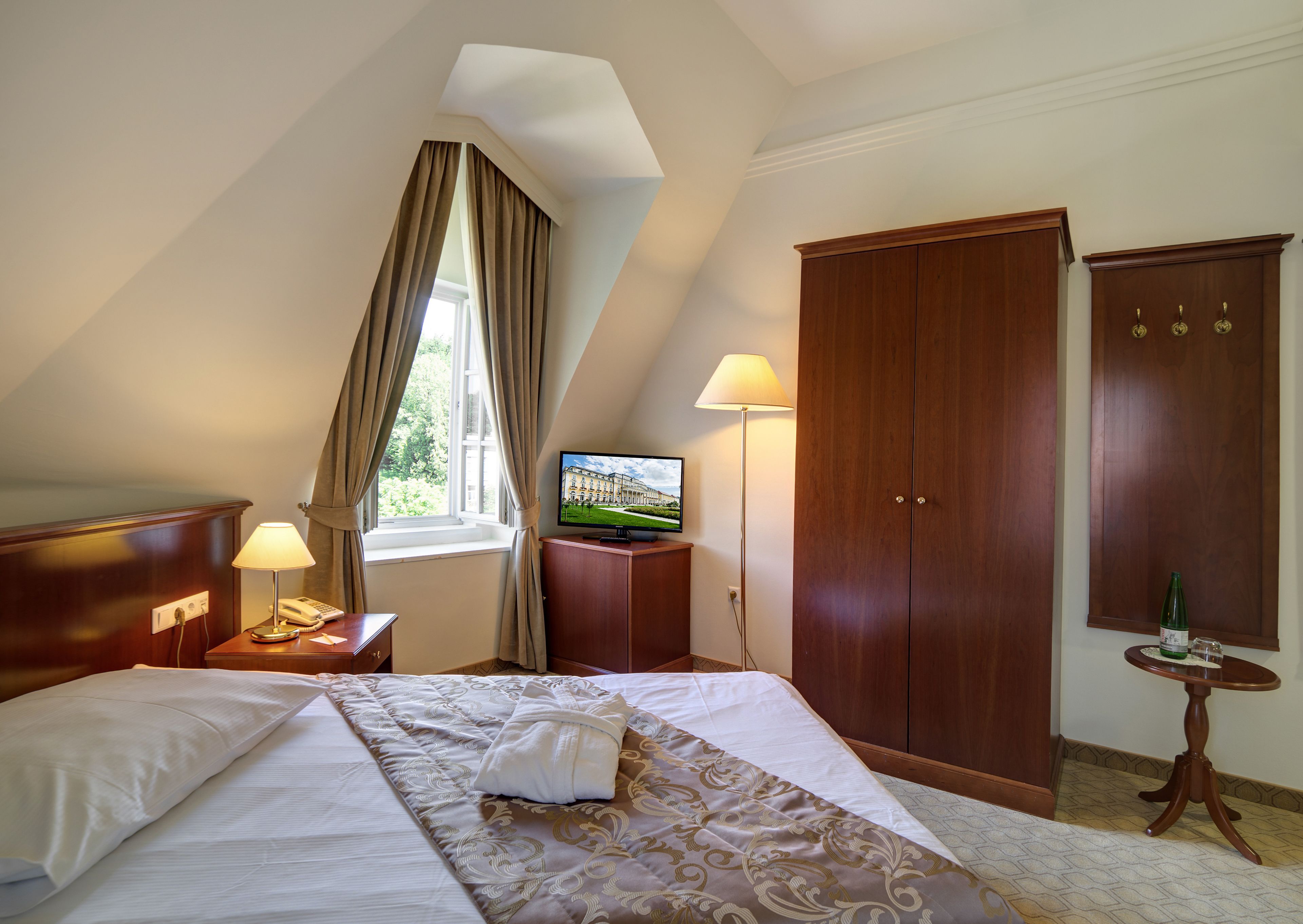 A hotel room with a bed, a television, a wardrobe, and a small table with a bottle.