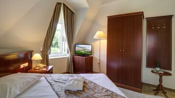 A hotel room with a bed, a television, a wardrobe, and a small table with a bottle.