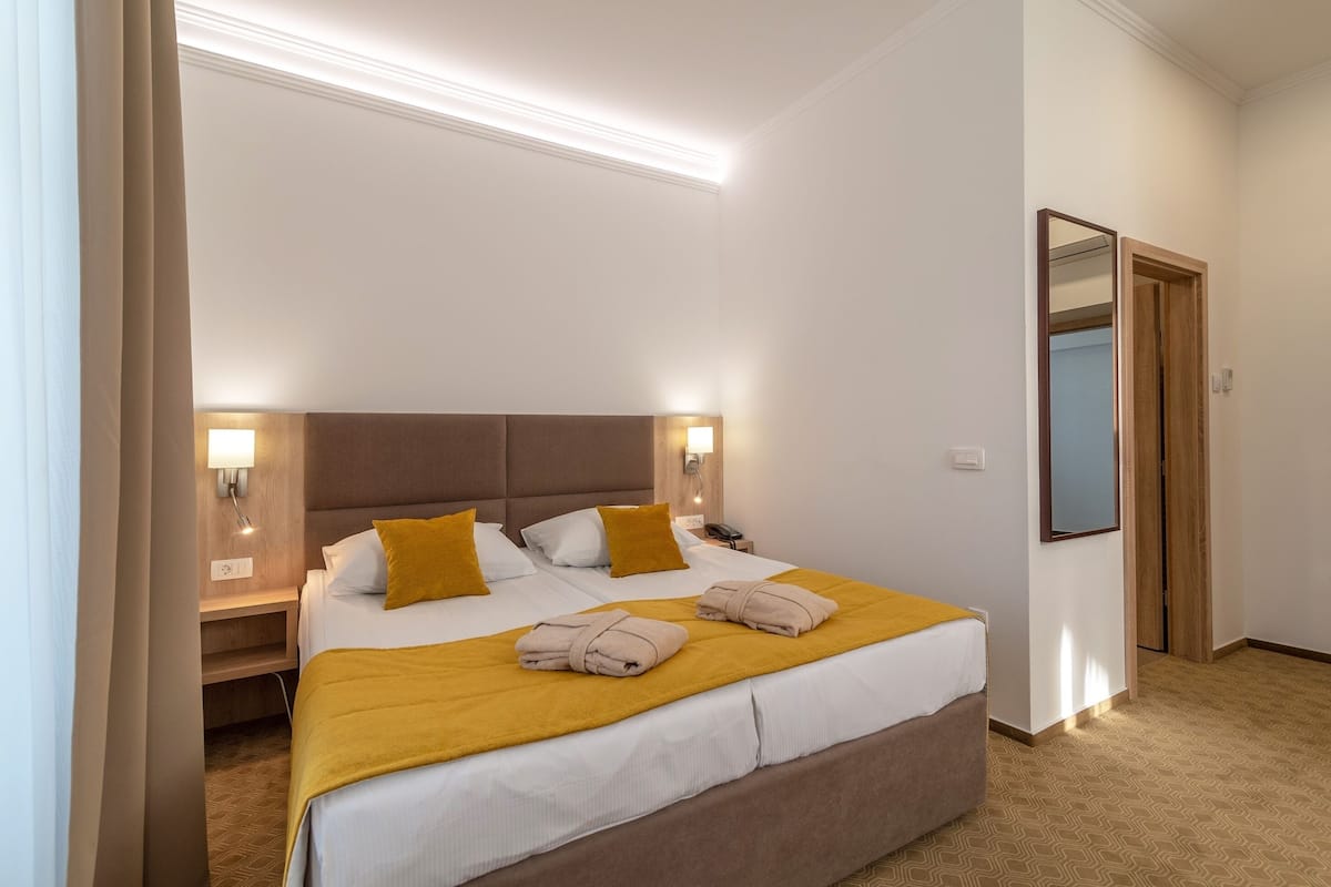 Ein Hotelzimmer mit einem großen Bett, zwei Nachttischen, einem Spiegel und einer Tür.