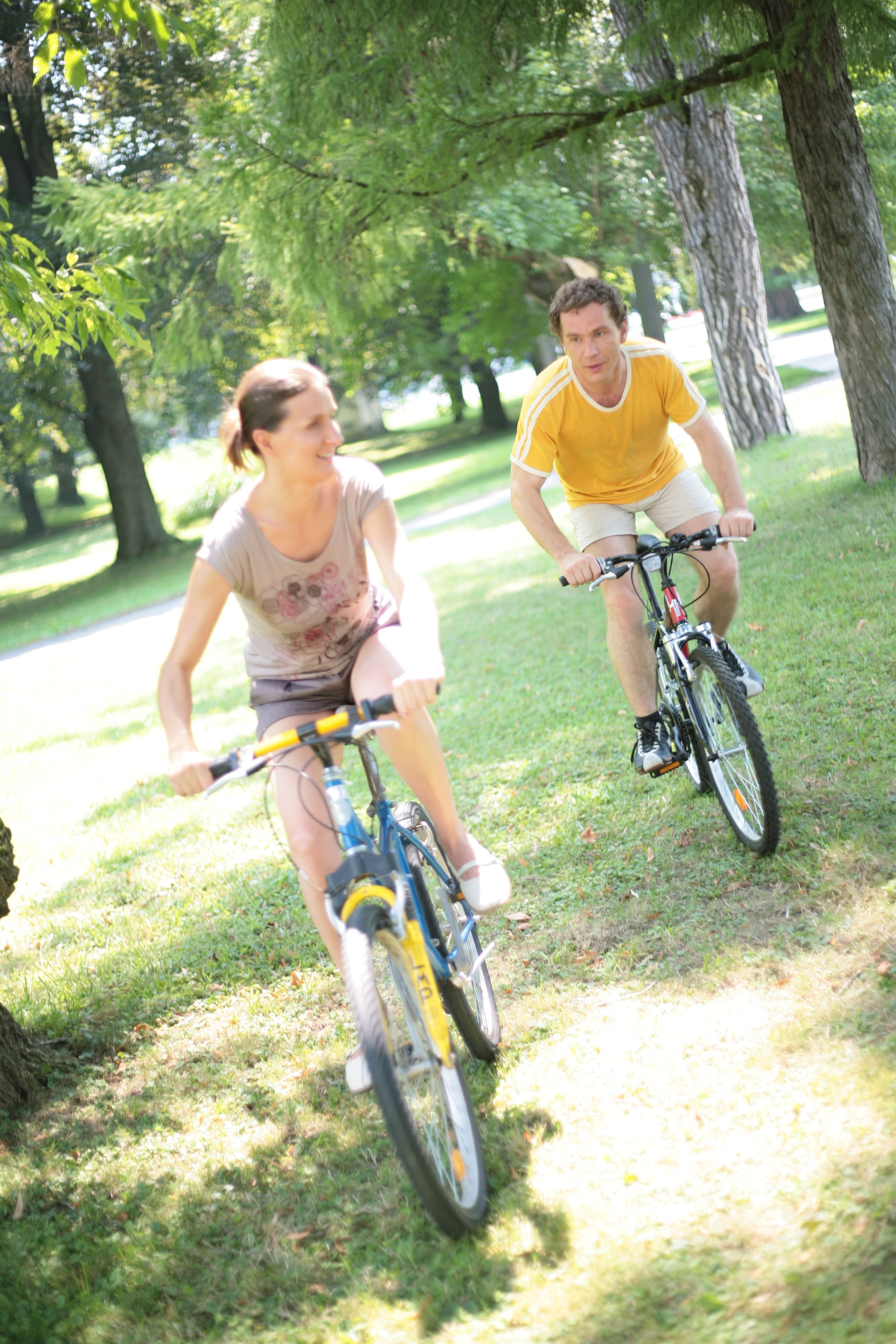 Two people riding bicycles on a grassy path in a park.