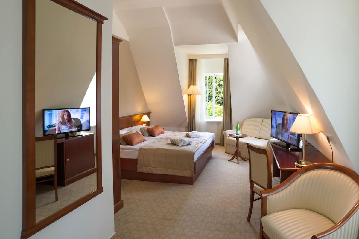 Ein Hotelzimmer mit einem Bett, einem Schreibtisch, einem Stuhl und zwei Fernsehern.