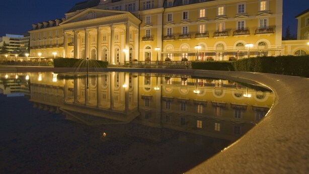 A large, classical building with a reflective pool in front, featuring symmetrical architecture and multiple balconies.