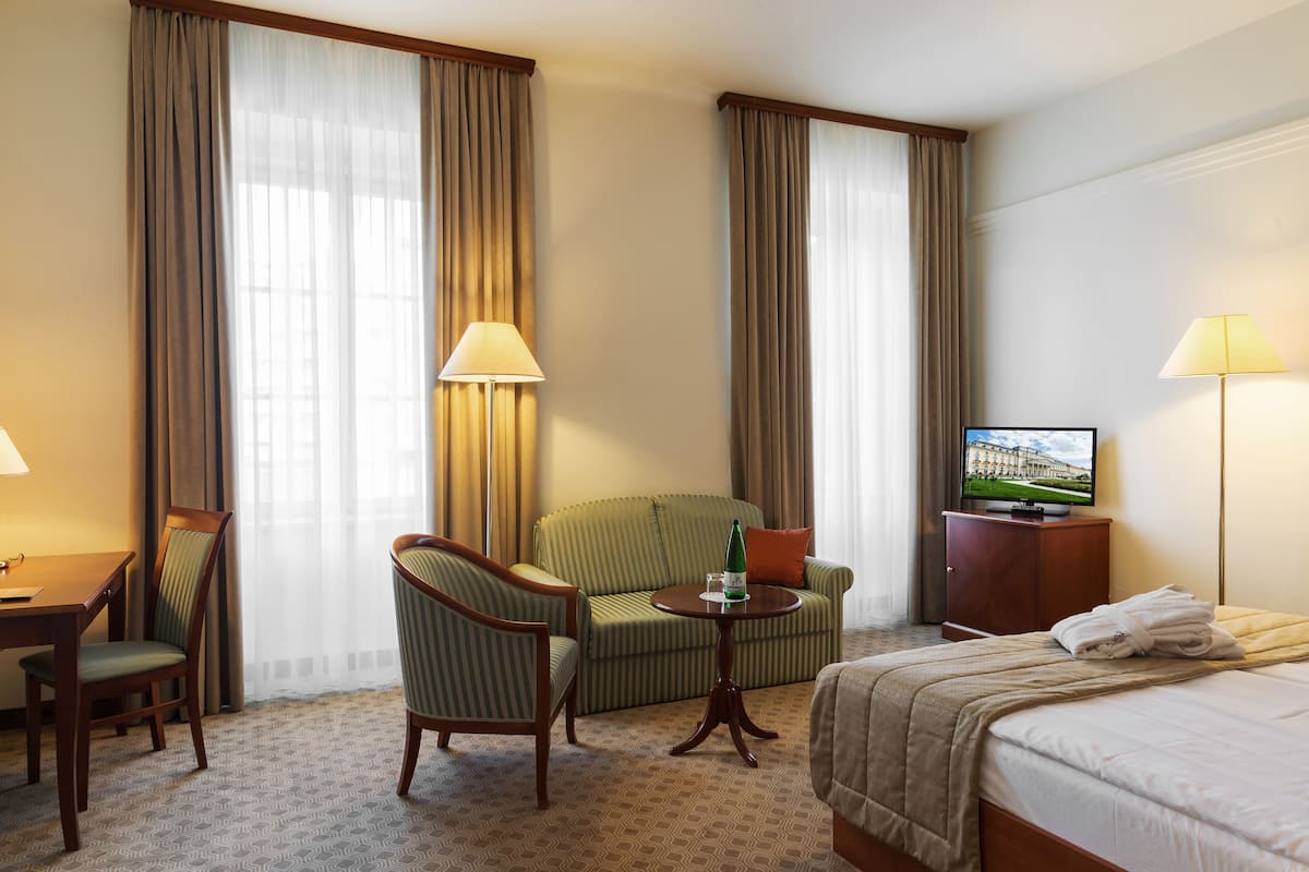 Ein Hotelzimmer mit Bett, Sofa, Fernseher und Schreibtisch mit Lampe.