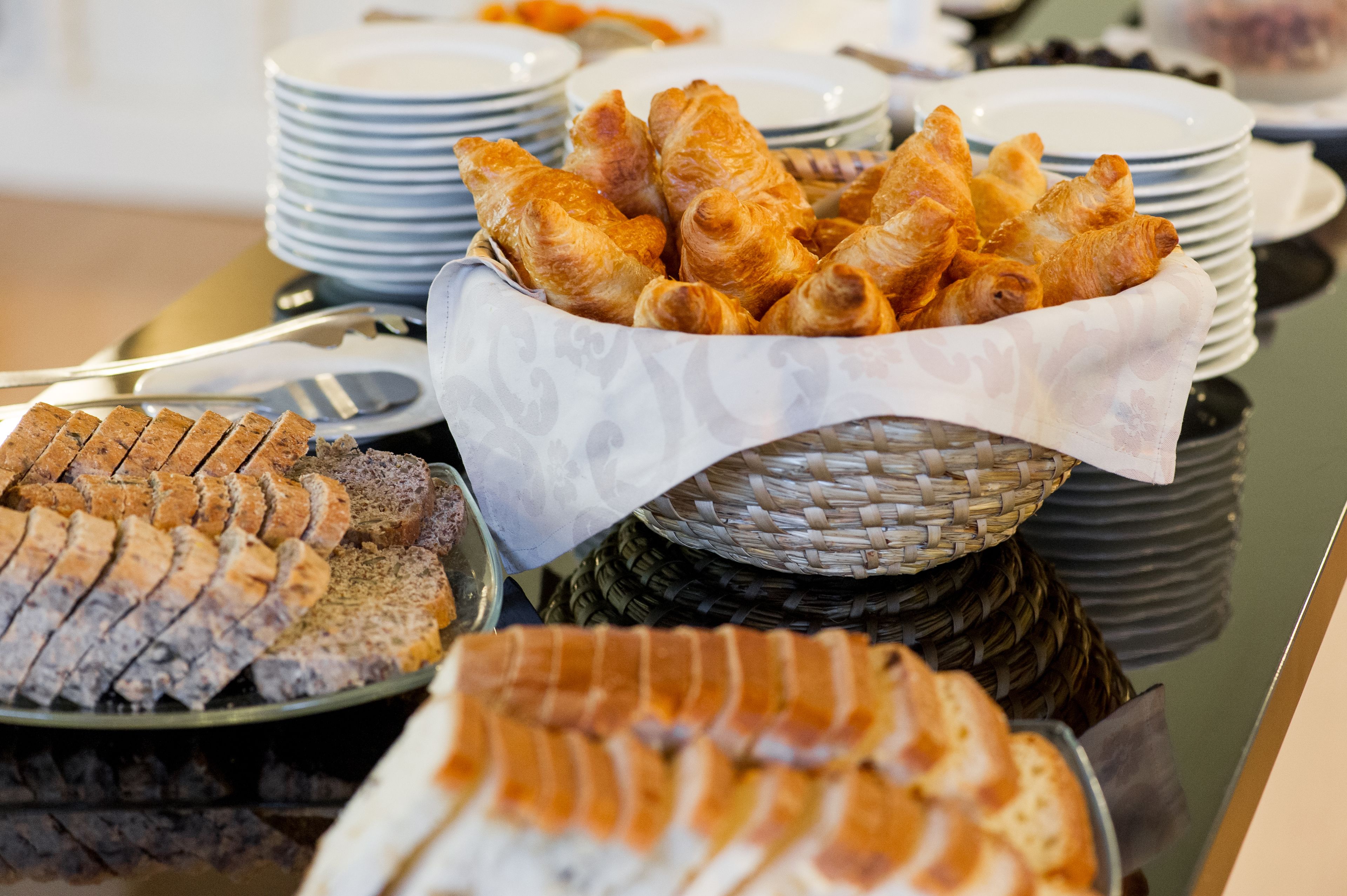 Buffet com diversos alimentos, incluindo croissants, pão fatiado e uma cesta de doces.