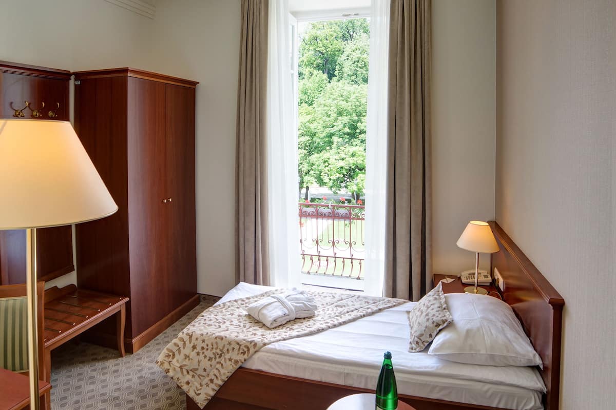 Ein Hotelzimmer mit Bett, Stuhl, Schreibtisch, Kleiderschrank und einem Fenster mit Blick ins Grüne.