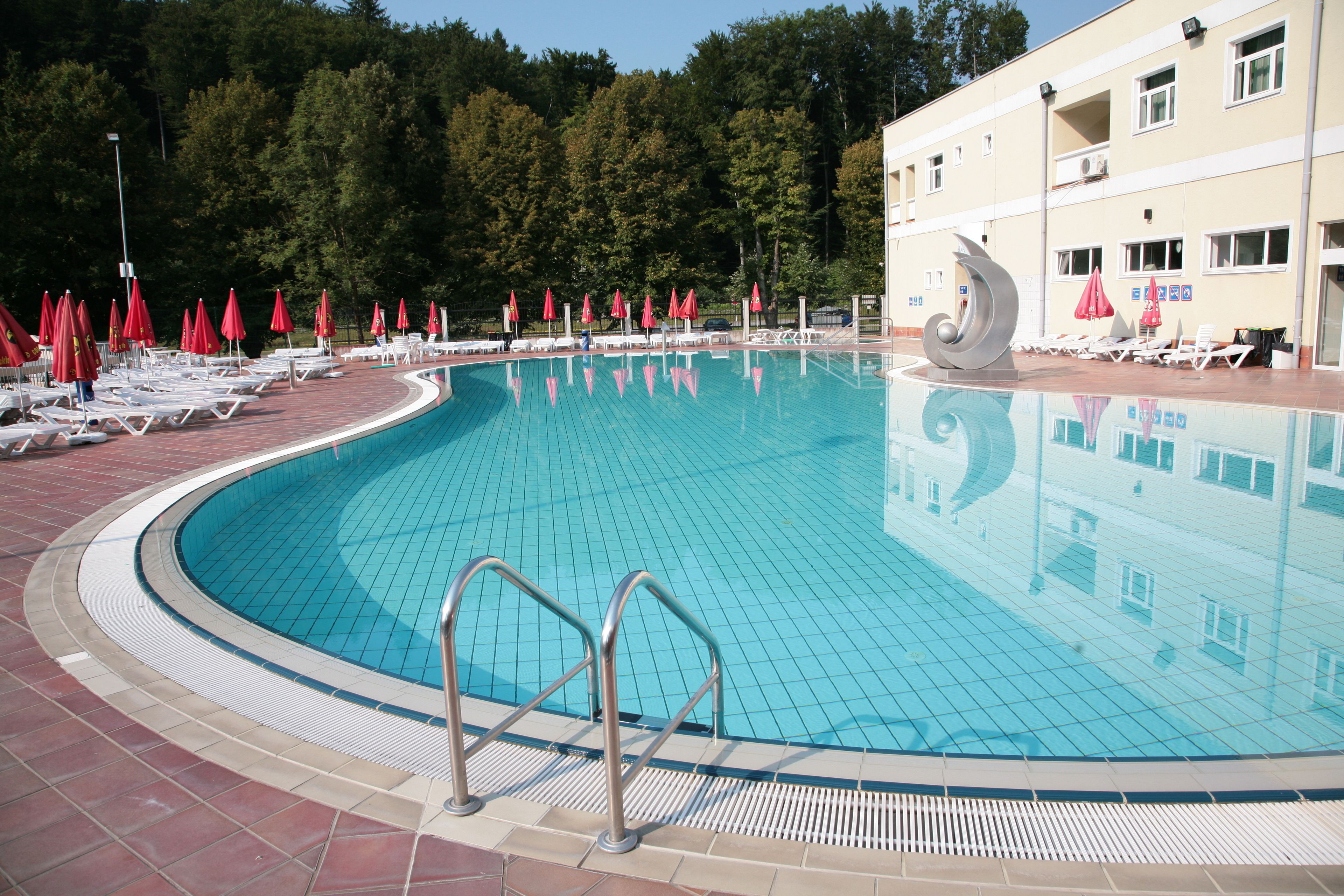 A swimming pool with tiled edges, sun loungers, and red umbrellas.
