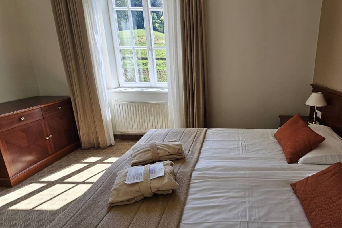 Ein Hotelzimmer mit einem großen Bett, einem Holzschrank, einem Nachttisch mit Lampe und einem Fenster mit Vorhängen.