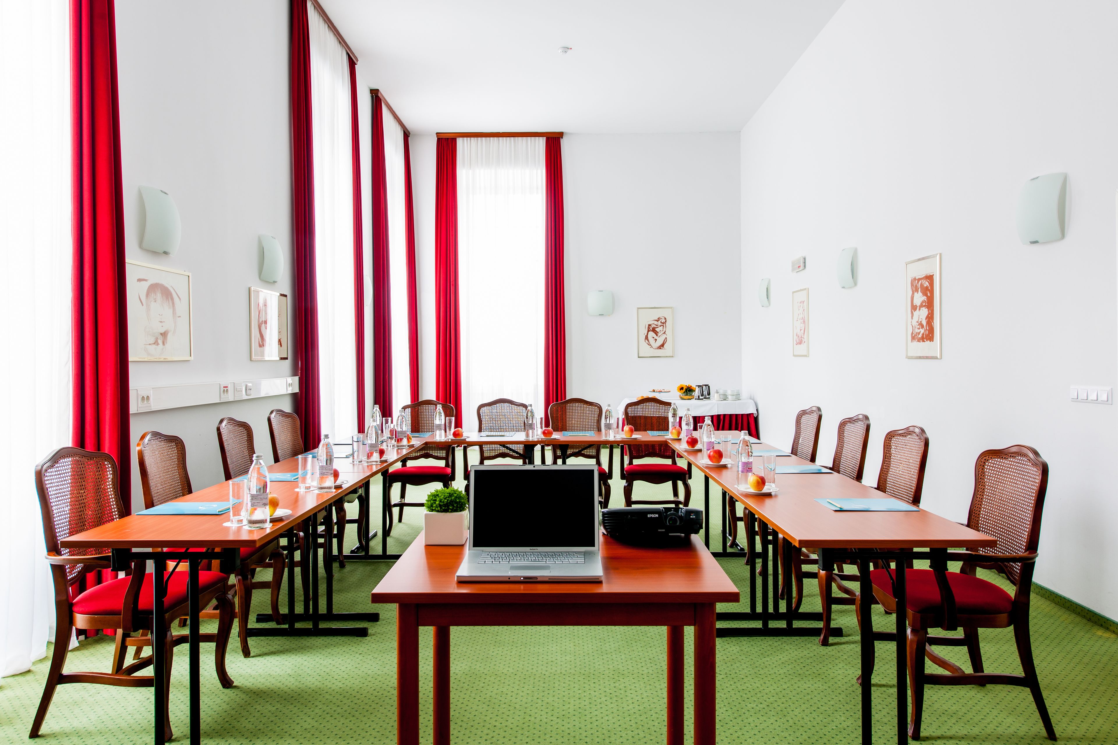Ein Konferenzraum mit einem langen Tisch, roten Stühlen und einem Laptop auf dem Tisch.